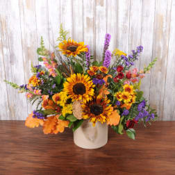 Mixed bouquet with sunflowers, red roses, and purple flowers in a cream vase
