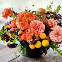 Orange and pink floral arrangement in a black vase with yellow fruit accents