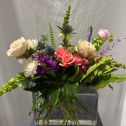 Mixed bouquet of roses, snapdragons, and purple flowers in a glass vase