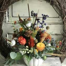 Mixed floral arrangement in a white pumpkin-shaped vase with orange, yellow, and purple blooms