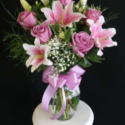 Pink roses and lilies in a glass vase with a pink ribbon