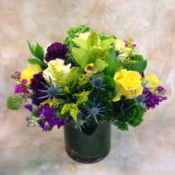 Mixed bouquet of yellow, purple, white, and green flowers in a dark vase