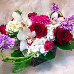 Bouquet of red roses, white orchids, and purple flowers in a glass vase