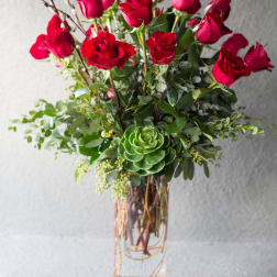 Red roses arranged in a clear glass vase with greenery and a succulent accent