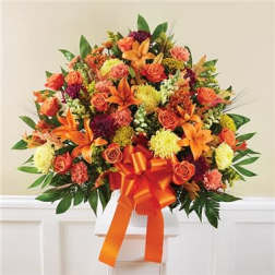 Orange and yellow mixed flower arrangement with a large ribbon in a white vase