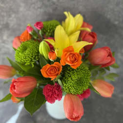 Bouquet of orange roses, yellow lilies, and pink tulips in a white vase