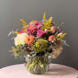 Mixed bouquet in a clear glass vase with pink, peach, white, and yellow blooms
