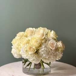 Low arrangement of cream roses and white hydrangeas in a clear glass cylinder vase