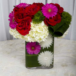 Red roses and pink daisies in a green vase with white hydrangeas
