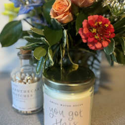 Small floral arrangement in a glass jar with roses and a red zinnia, beside candles