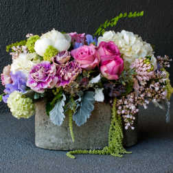 Mixed bouquet of pink roses, purple carnations, and white blooms in a concrete container