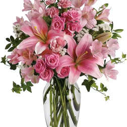Pink lilies and roses arranged in a clear glass vase