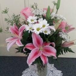 Pink lilies and white daisies arranged in a glass vase