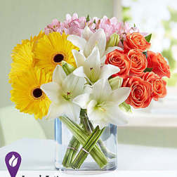 Bouquet of yellow gerbera daisies, white lilies, and orange roses in a glass vase