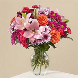 Bouquet of pink lilies, roses, and daisies in a clear glass vase