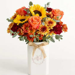Bouquet of sunflowers, roses, and mums in a white vase with a ribbon