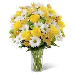 Yellow roses, white daisies, and green button mums arranged in a clear glass vase