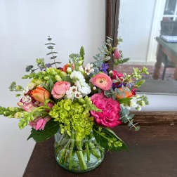 Mixed bouquet of pink, white, orange, and green flowers in a glass vase