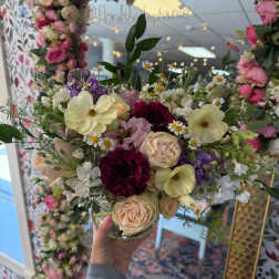 Mixed bouquet of pastel roses, daisies, and purple blooms in a glass vase