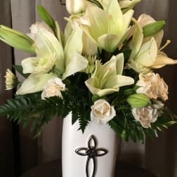 White lilies and cream roses in a tall white vase with a cross emblem