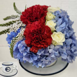 Bouquet of red carnations, white roses, and blue hydrangeas in a glass bowl