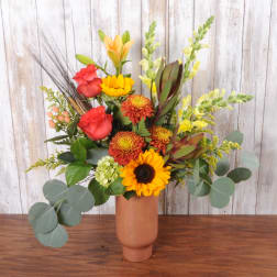 Mixed bouquet in a tall copper vase with red, yellow, and orange flowers