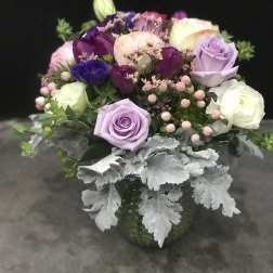 Bouquet of purple, pink, and white roses with silver foliage in a vase
