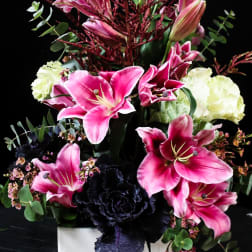 Pink lilies and dark purple flowers in a white square vase