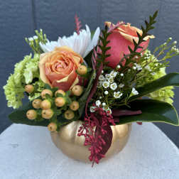 Peach and pink roses arranged in a gold pumpkin vase