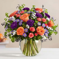 Bouquet of orange roses, purple flowers, and pink carnations in a glass vase