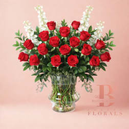 Red roses arranged in a clear glass vase with white accent flowers