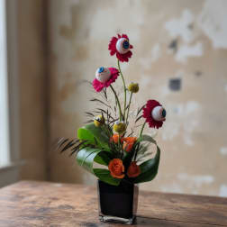 Small floral arrangement with orange roses and pink daisy-like blooms in a black vase