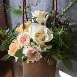 Cream and blush roses in a brown gift bag with greenery