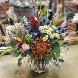 Mixed bouquet in a clear glass vase with daisies and spiky blue flowers