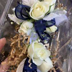 White rose corsage with navy ribbon in clear packaging