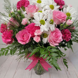 Pink roses, white daisies, and carnations in a glass vase with a polka-dot ribbon