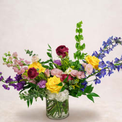 Mixed bouquet of roses, snapdragons, and blue delphinium in a glass vase