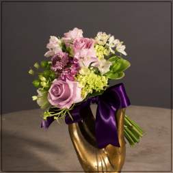 Pink and white bouquet in a gold vase with a purple ribbon