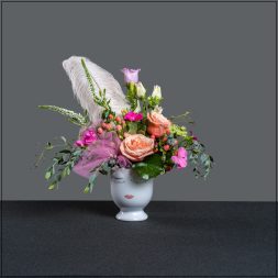 Pink and peach floral arrangement in a white face vase with a feather accent