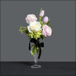 Pink and white flowers arranged in a clear glass vase with a black ribbon