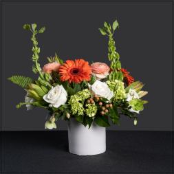 Mixed floral arrangement in a white vase with orange and white blooms