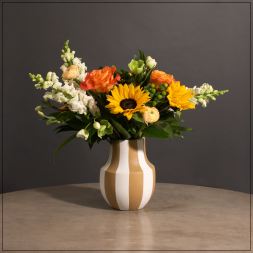 Bouquet of sunflowers, orange roses, and white snapdragons in a striped vase