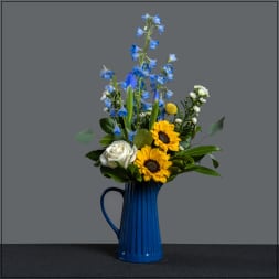Blue delphiniums and sunflowers in a blue pitcher vase