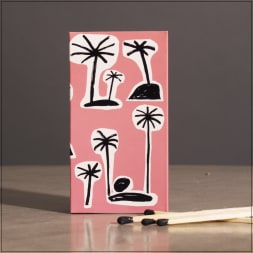 Pink matchbox with black palm tree drawings and matches beside it