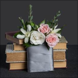 Pink and white roses with white lilies arranged over stacked books