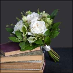 White rose bouquet with green accents resting on stacked books