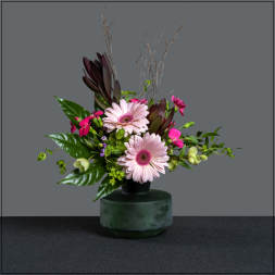 Pink gerbera daisies in a dark green vase with glossy leaves