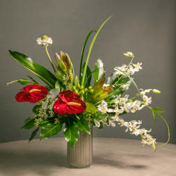 Tropical floral arrangement with red anthuriums and white orchids in a ribbed vase