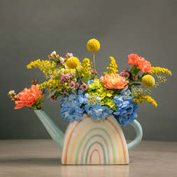 Colorful flowers arranged in a pastel watering can vase with a rainbow design