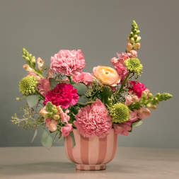 Pink and peach mixed flower arrangement in a striped pink vase